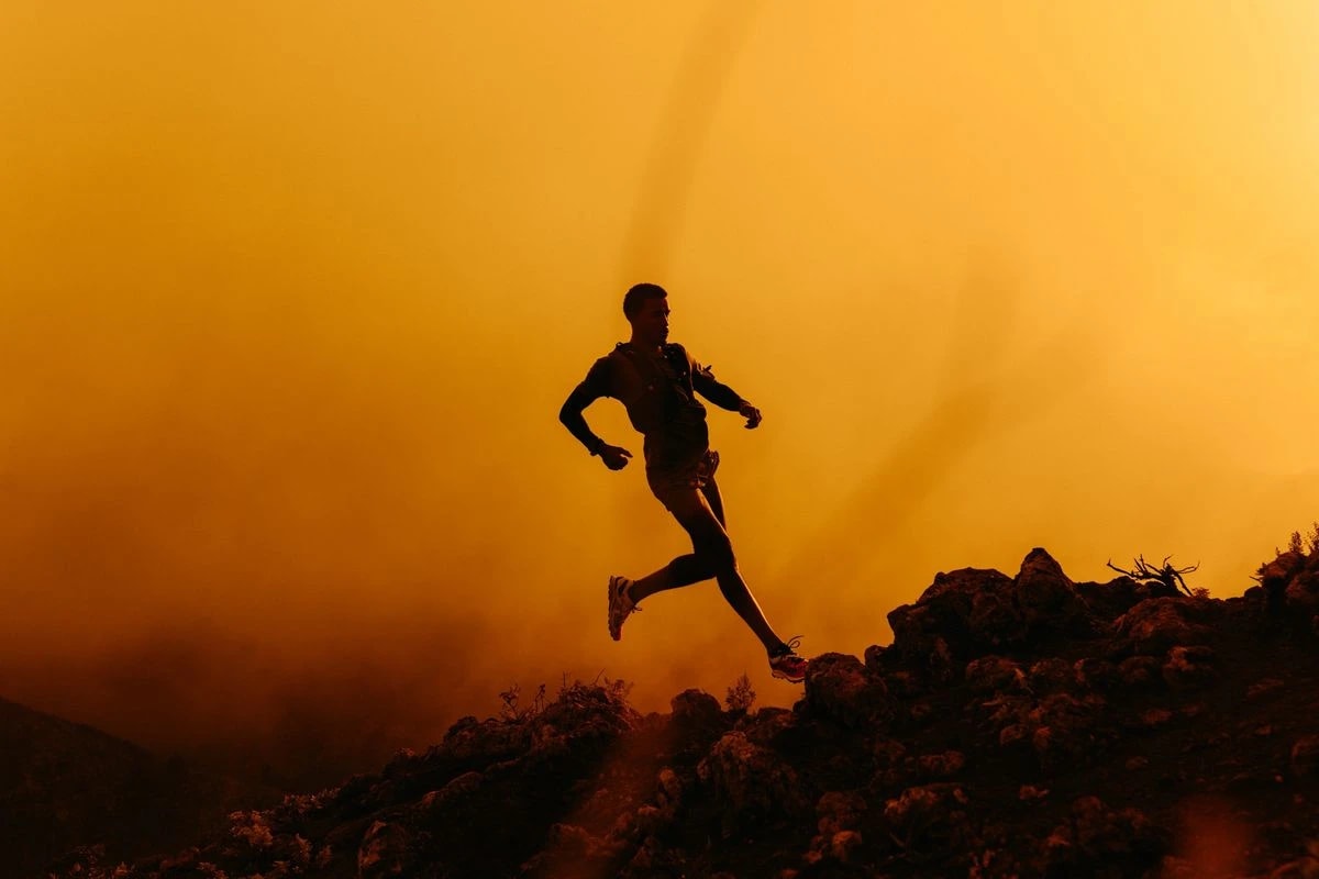 A trail runner silhouetted against an orange sky